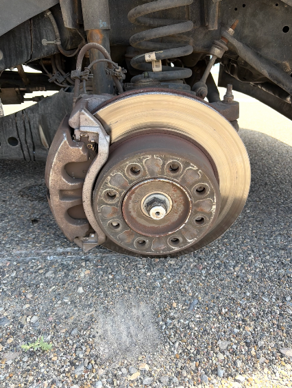 Brake rotor and caliper on a car raised on a jack stand in a driveway