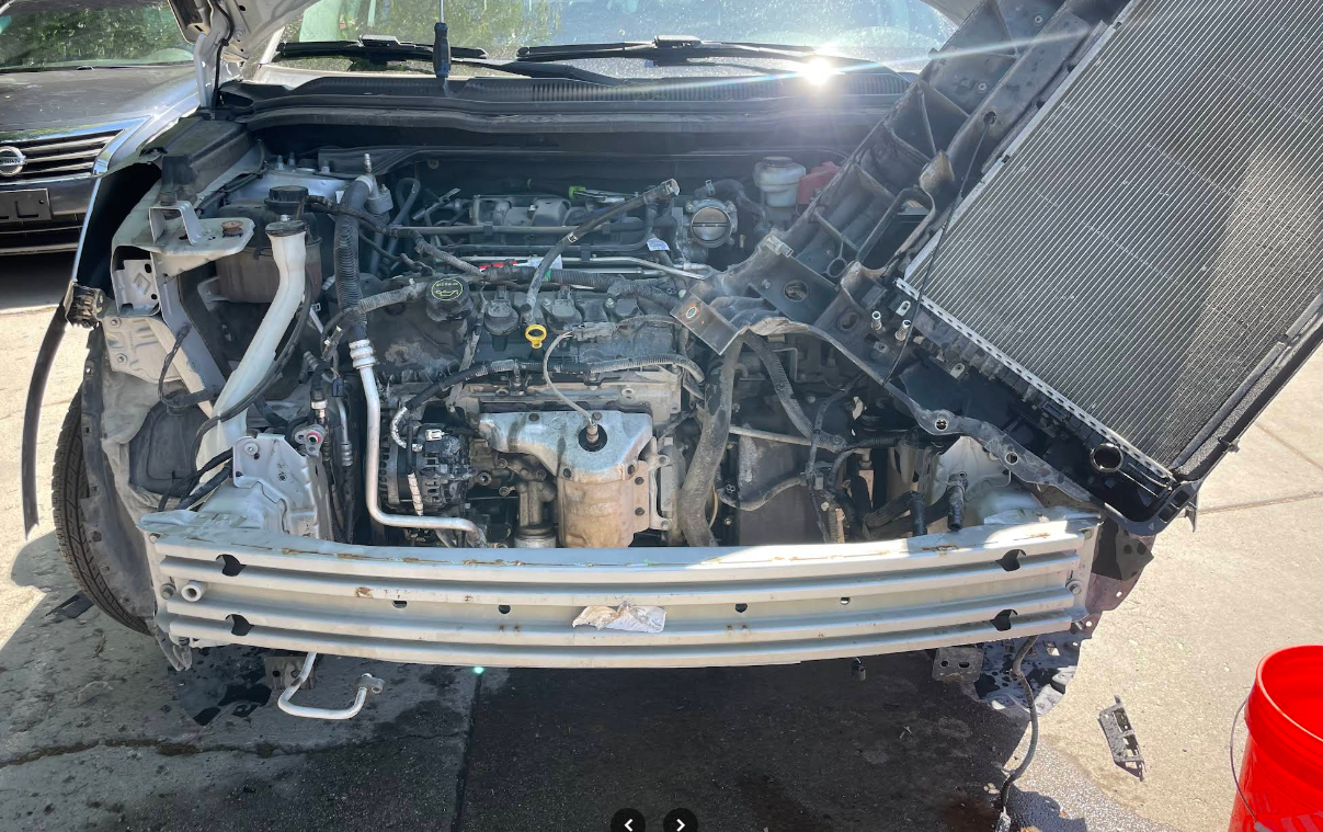 Front end of a car opened up for radiator and engine work in a driveway